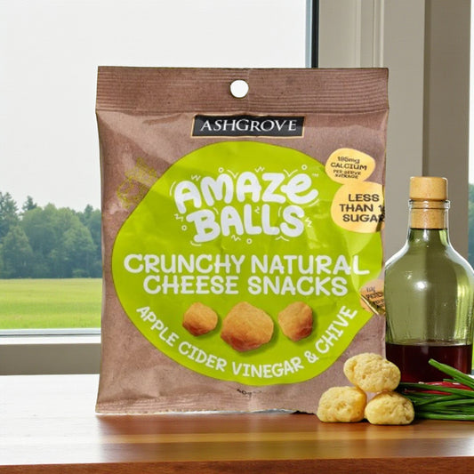 Packaging of Ashgrove Cheese Amaze Balls crunchy natural cheese snacks with a bottle of apple cider vinegar and chives on a table.