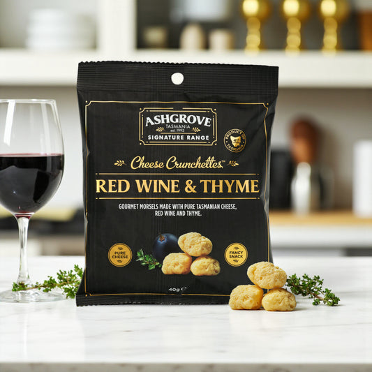 Packaging of Ashgrove Cheese Tasmania Crunchettes Red Wine & Thyme with a glass of red wine and snacks on a table.