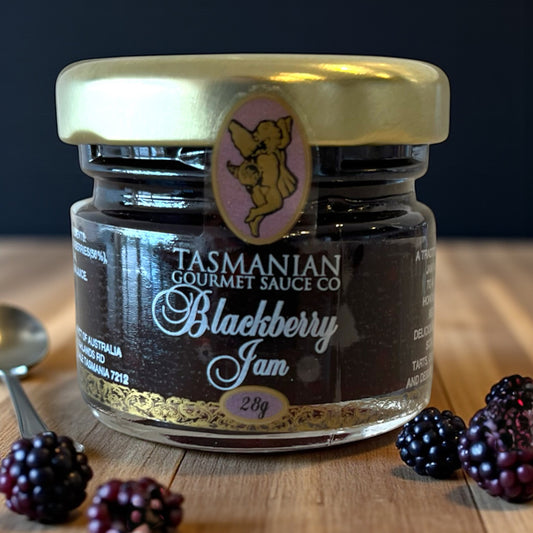 Jar of Tasmanian Gourmet Sauce Co Blackberry Jam on a wooden surface with blackberries.
