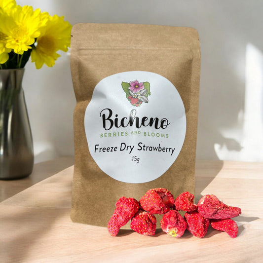A package of Bicheno Tasmania freeze-dried strawberries with some strawberries scattered in front, on a table with a vase of yellow flowers in the background.