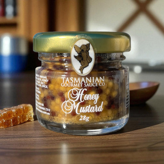 A jar of Tasmanian Honey Mustard sauce with a weight of 28g, placed on a wooden surface with a piece of honeycomb.