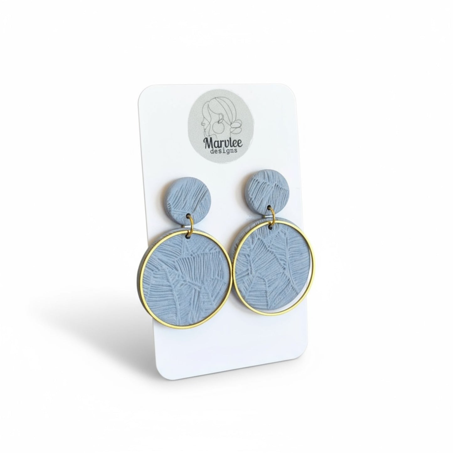 Close-up of Andy earrings showing botanical leaf impressions in blue-grey polymer clay with gold hoop frame