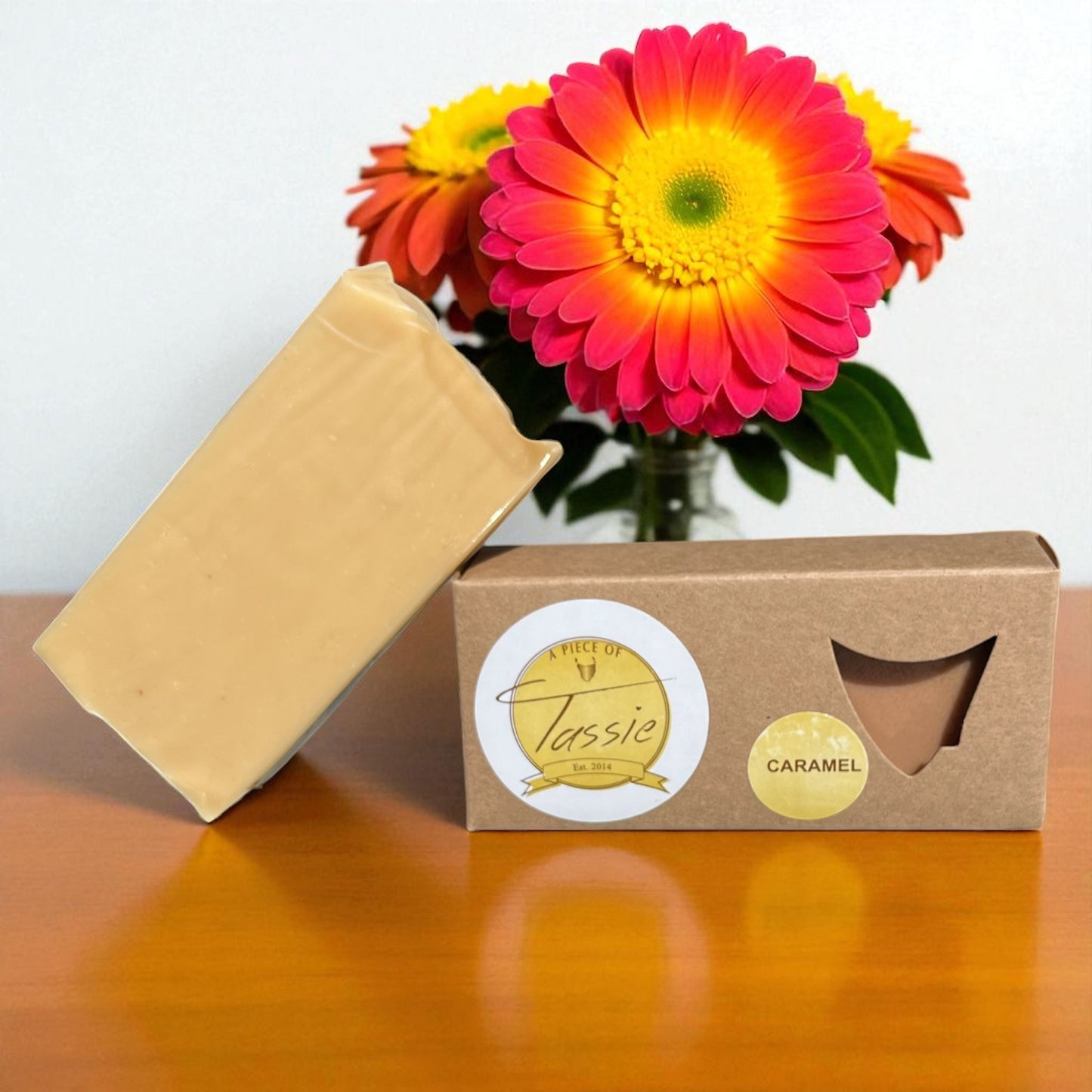 Bar of Tasmanian caramel fudge on a wooden surface with bright flowers in the background.