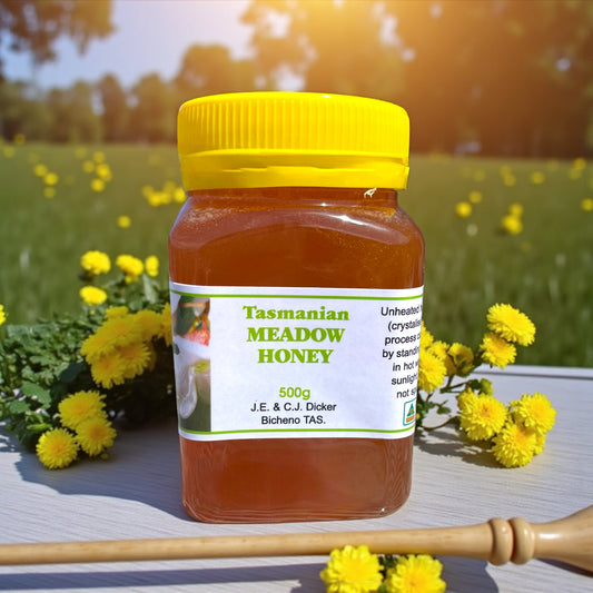 Jar of Tasmanian Meadow Honey with a yellow lid on a wooden surface with flowers in the background