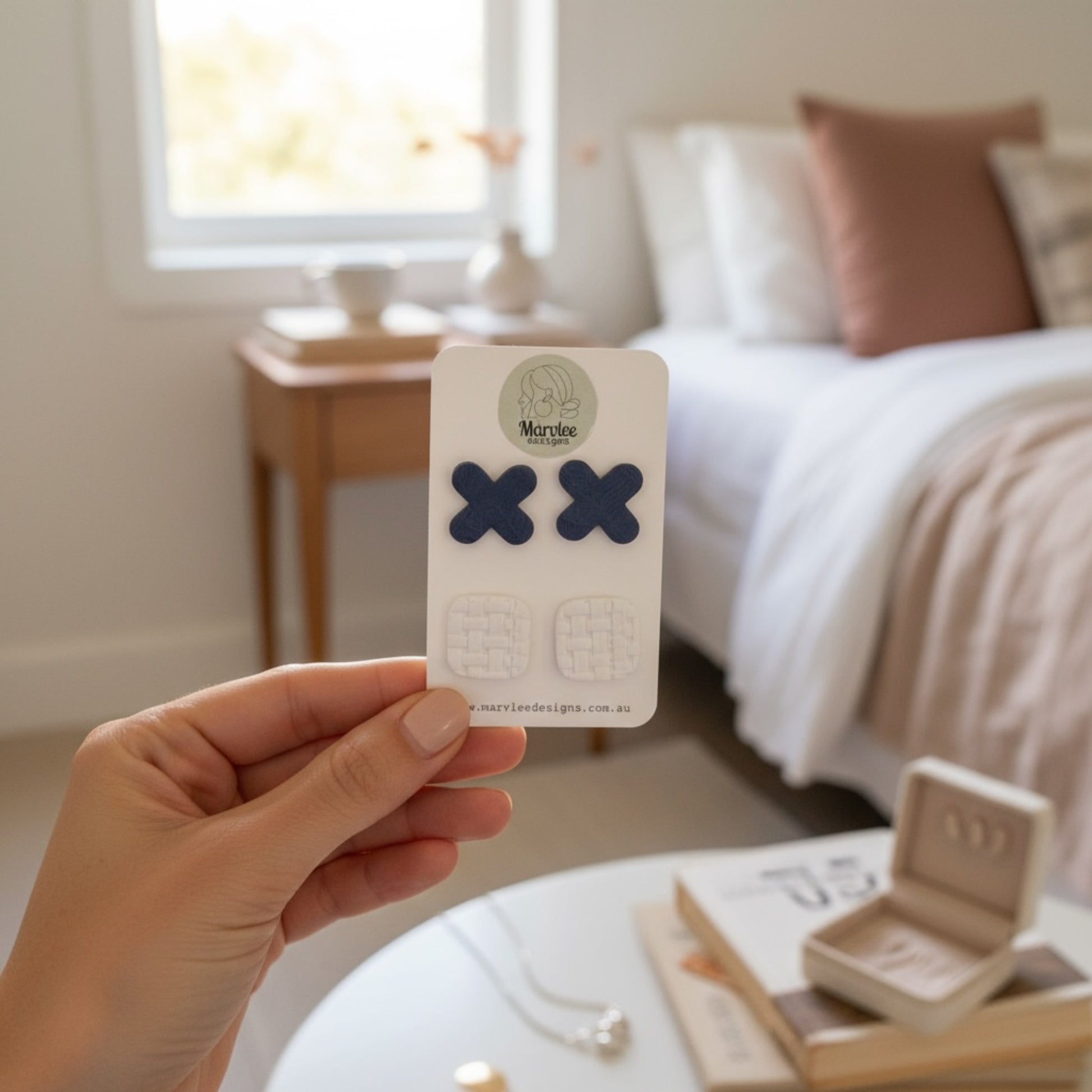 Hand holding a card with Tasmanian handcrafted earrings in a bedroom setting.