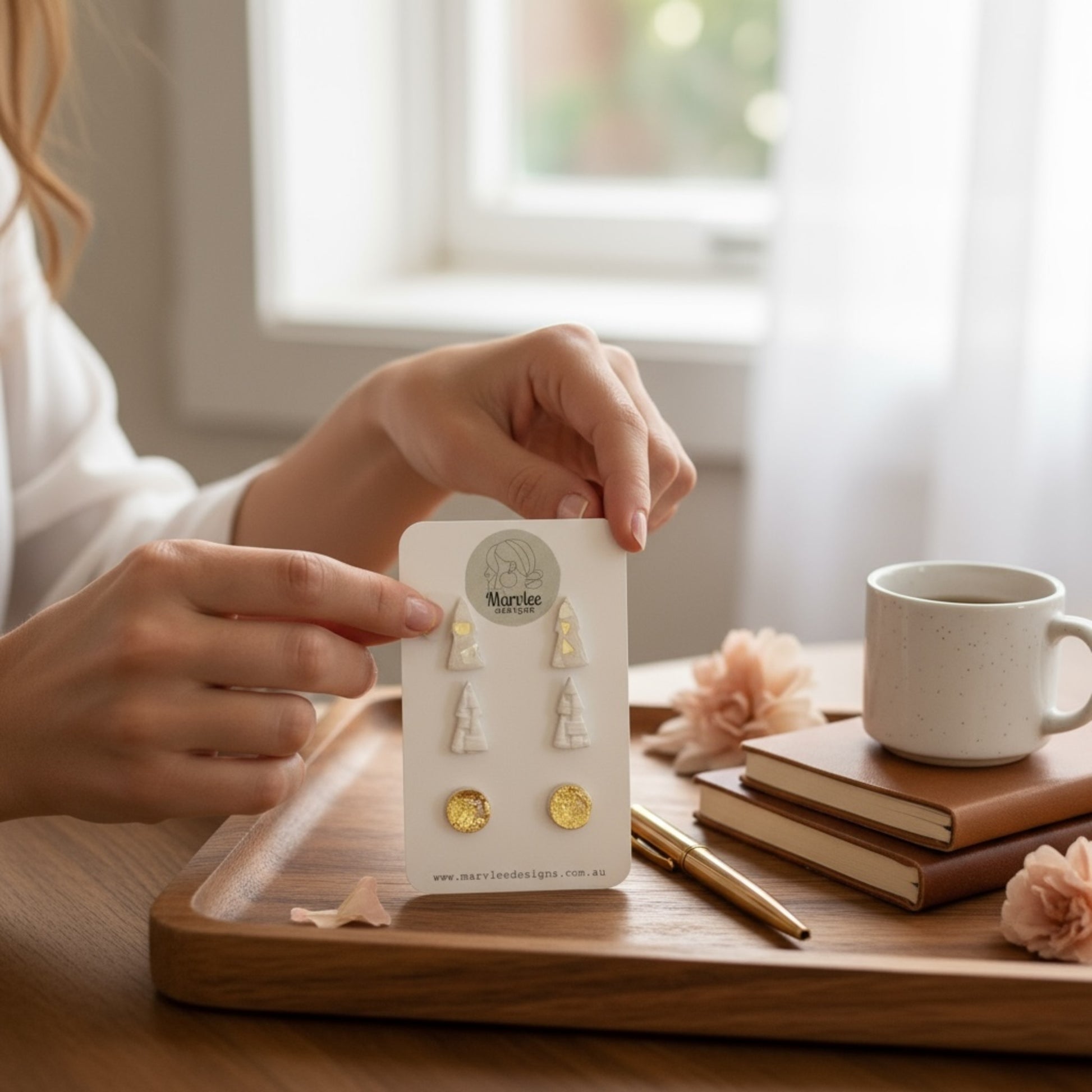 Person holding a card with Tasmanian earrings on a wooden tray with a cup and books in the background