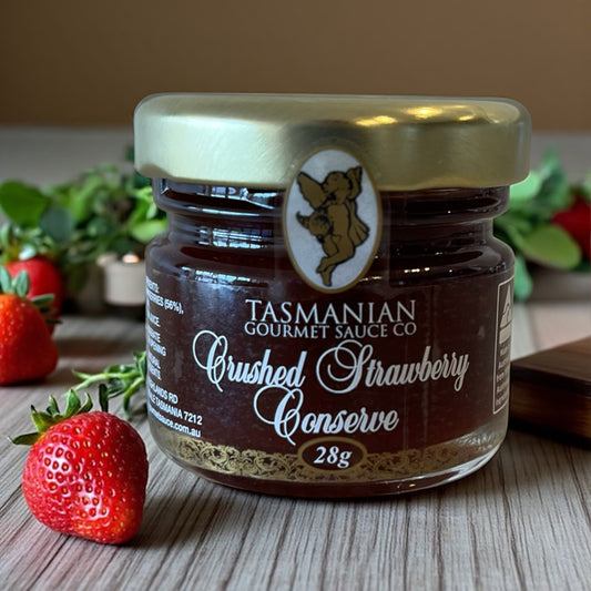Jar of Tasmanian Gourmet Sauce Co. Crushed Strawberry Conserve with strawberries on a wooden surface.