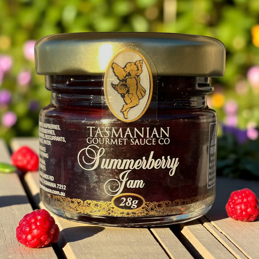 Jar of Tasmanian Gourmet Sauce Co Summerberry Jam with raspberries on a wooden surface.