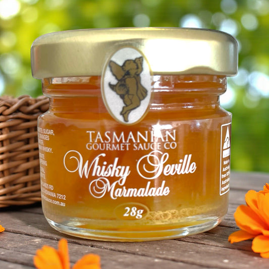 Jar of Tasmanian Gourmet Sauce Company Whisky Seville Marmalade on a wooden surface with greenery in the background.
