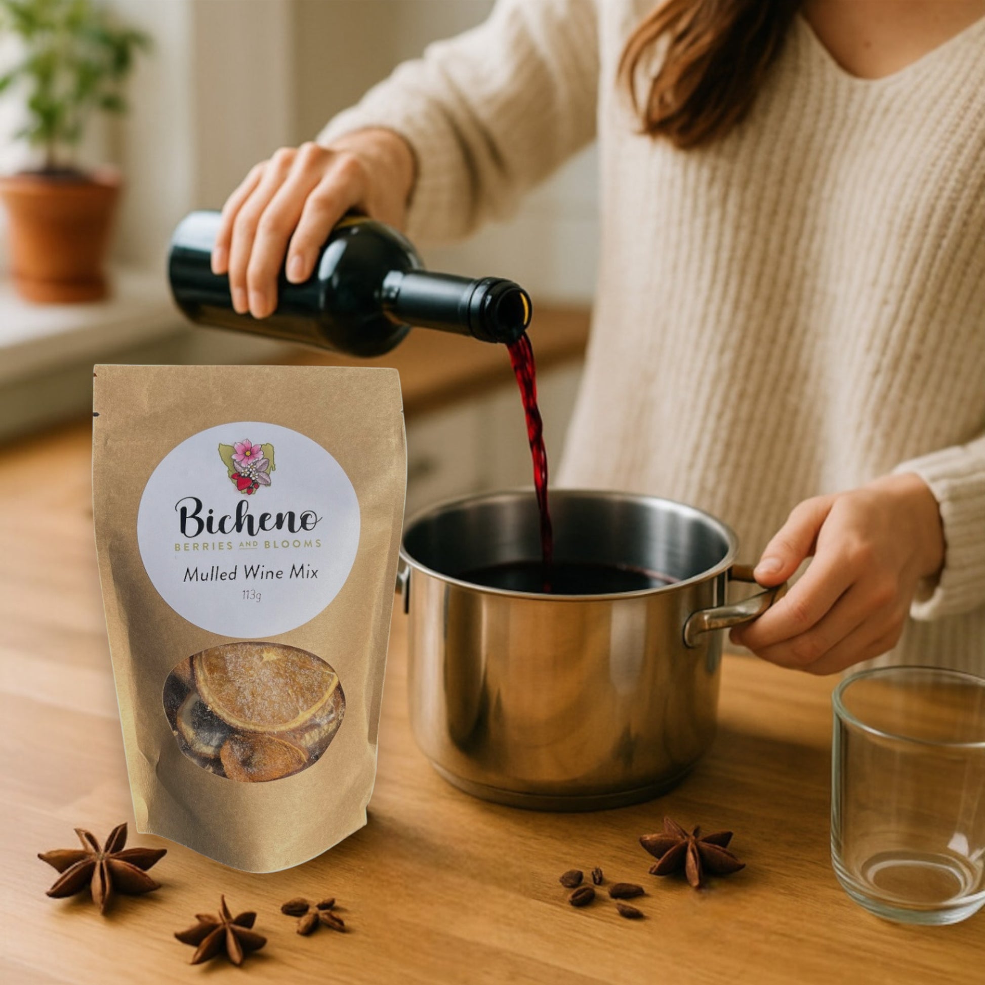 Person pouring red wine into a pot with Bicheno Berries & Blooms Tasmania Mulled Wine Mix packaging on a wooden surface.