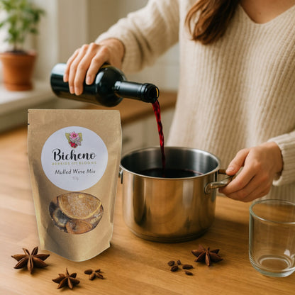 Person pouring red wine into a pot with Bicheno Berries & Blooms Tasmania Mulled Wine Mix packaging on a wooden surface.