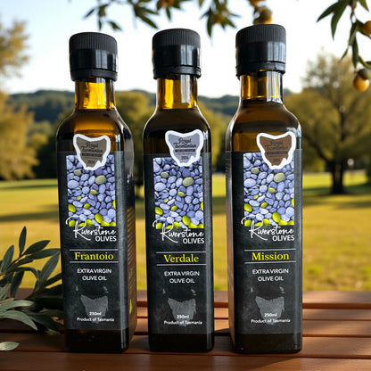 Three bottles of Tasmanian Riverstone Olives extra virgin olive oil with labels on a wooden surface outdoors.