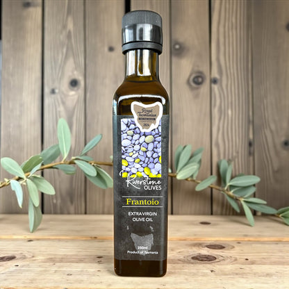 Bottle of Riverstone Olives Tasmanian Frantoio Extra Virgin Olive Oil on a wooden surface with an olive branch.