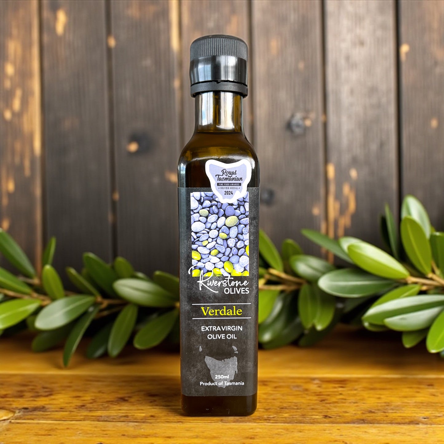 Bottle of Verdale Tasmanian Extra Virgin Olive Oil with a decorative background of green olive leaves.