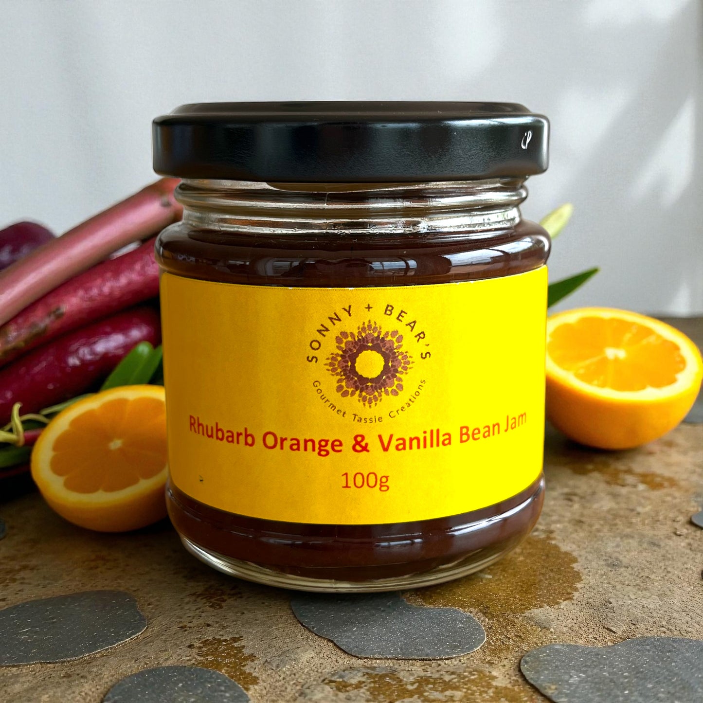 Jar of Sonny & Bear's Tasmanian Rhubarb Orange & Vanilla Bean Jam with oranges and rhubarb in the background.