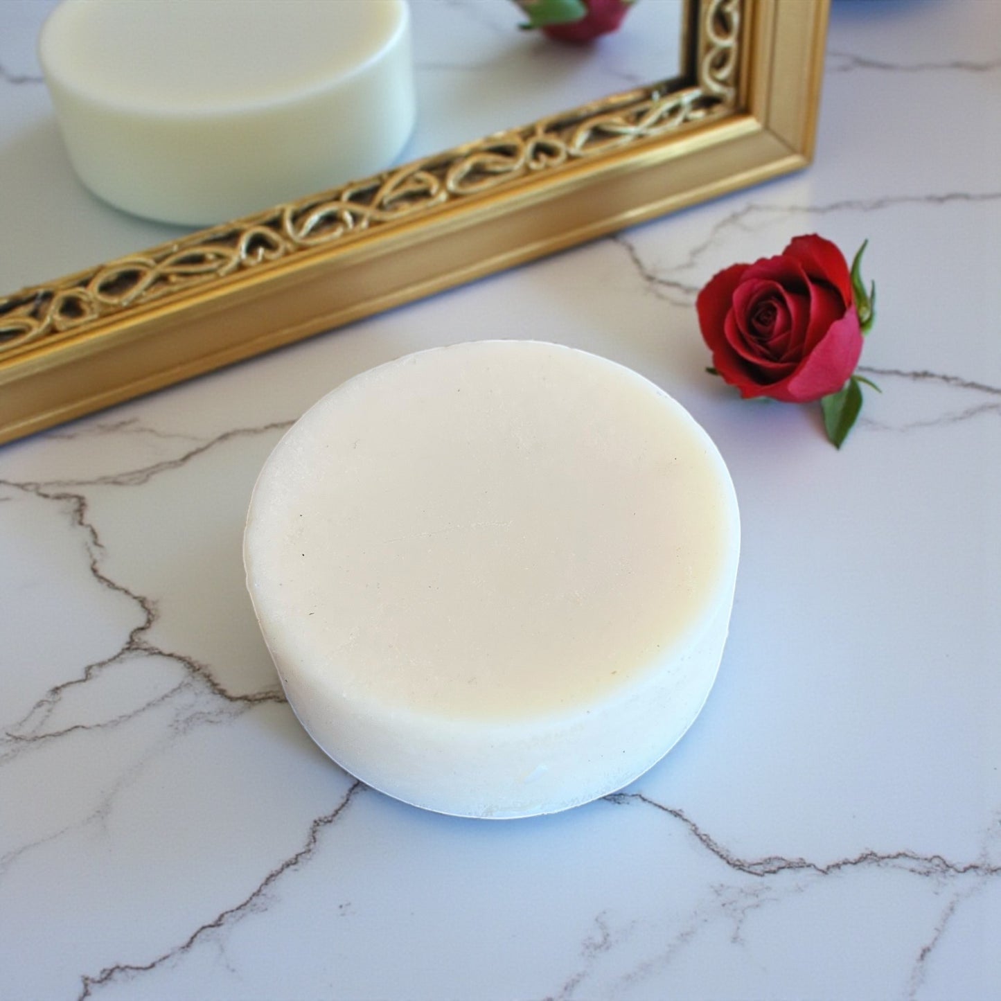 Natural solid hand moisturiser with Tasmanian tallow, beeswax and shea butter on a marble surface with a gold-framed mirror and red rose in the background.
