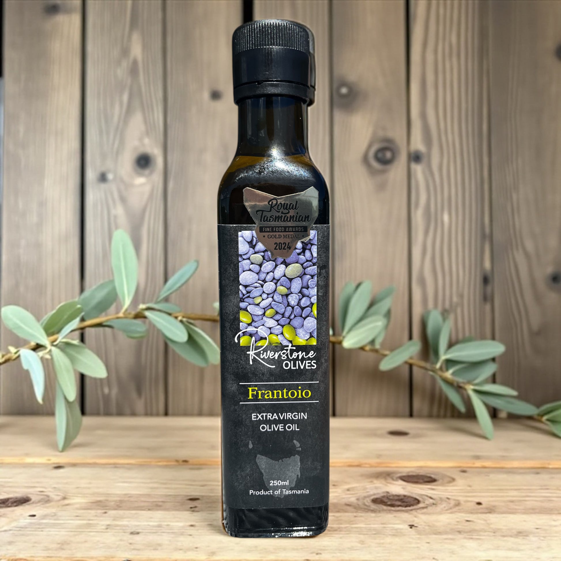 Bottle of Riverstone Olives Tasmanian Frantoio Extra Virgin Olive Oil on a wooden surface with an olive branch.