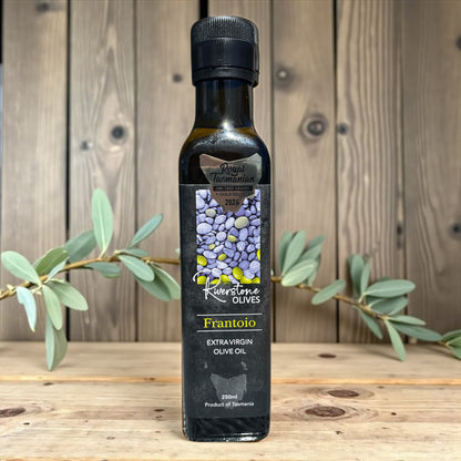 Bottle of Riverstone Olives Tasmanian Frantoio Extra Virgin Olive Oil on a wooden surface with an olive branch.