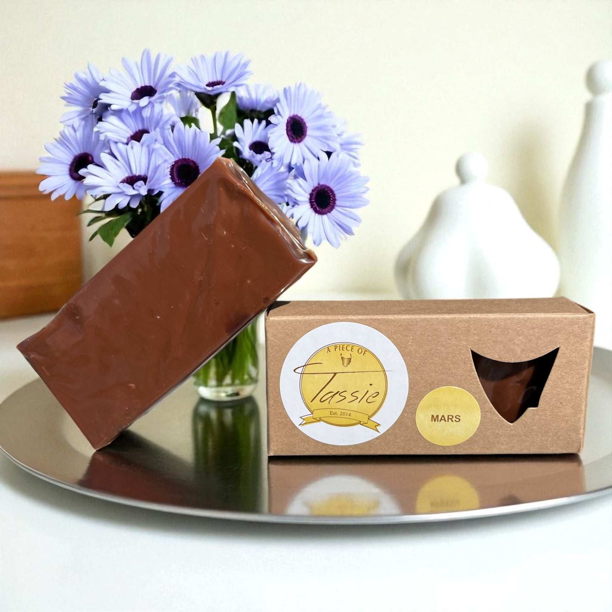 Tasmanian Chocolate fudge on a reflective surface with flowers in the background.