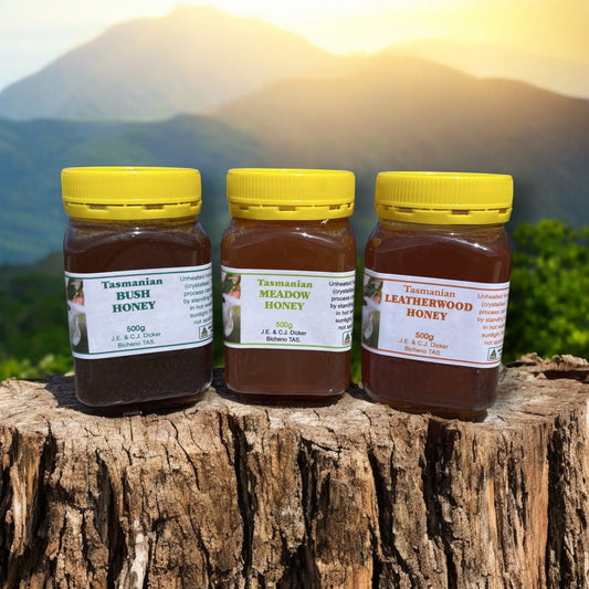 Three jars of Tasmanian honey with labels on a wooden log against a mountainous background