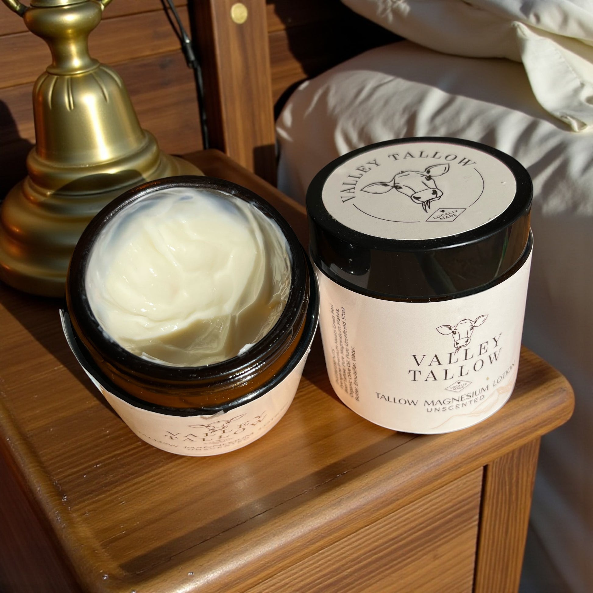 Tasmanian Valley Tallow Magnesium Lotion unscented with open lid showing rich tallow lotion texture on wooden bedside table